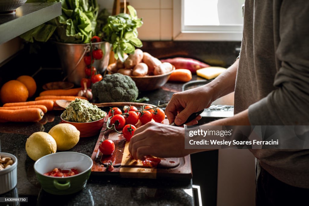Human hands slicing tomatoes over a wooden table for a vegan meal