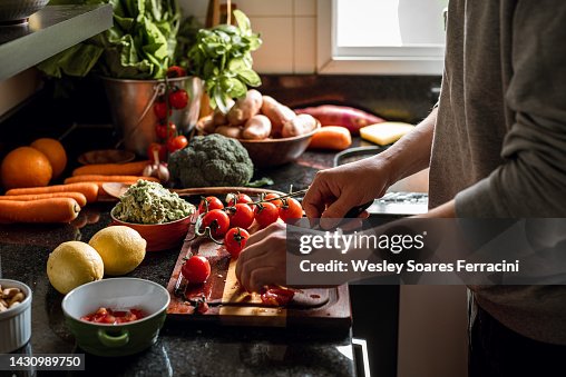 Human hands slicing tomatoes over a wooden table for a vegan meal Human hands slicing tomatoes over a wooden table for a vegan meal