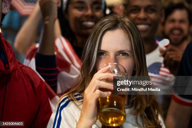 young woman drinking beer at sports bar while watching usa national team game surrounded by friends - crowd cheering bar stock pictures, royalty-free photos & images