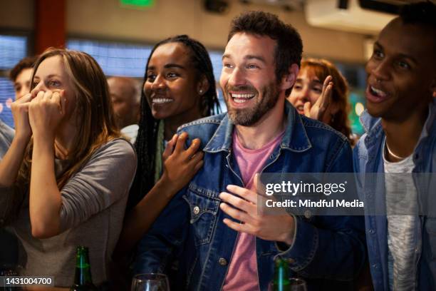 group of friends having a good time at sports bar while watching their team's game on tv - crowd cheering bar stock pictures, royalty-free photos & images