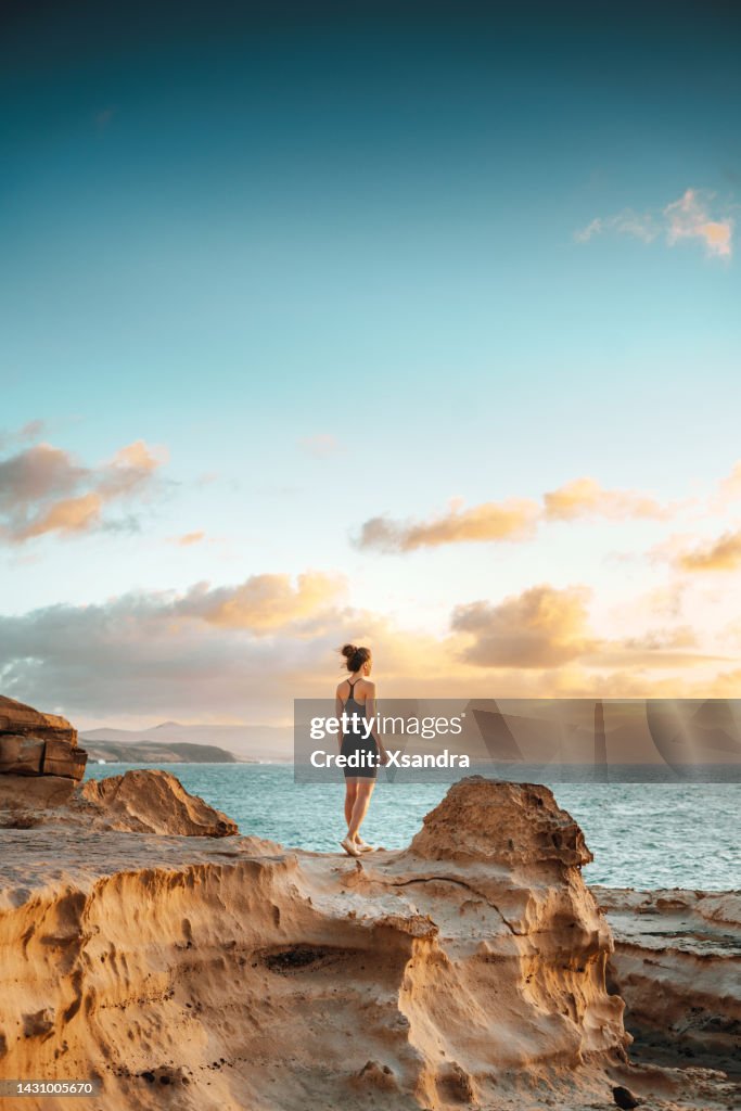 Woman standing on a cliff overlooking spectacular sunset