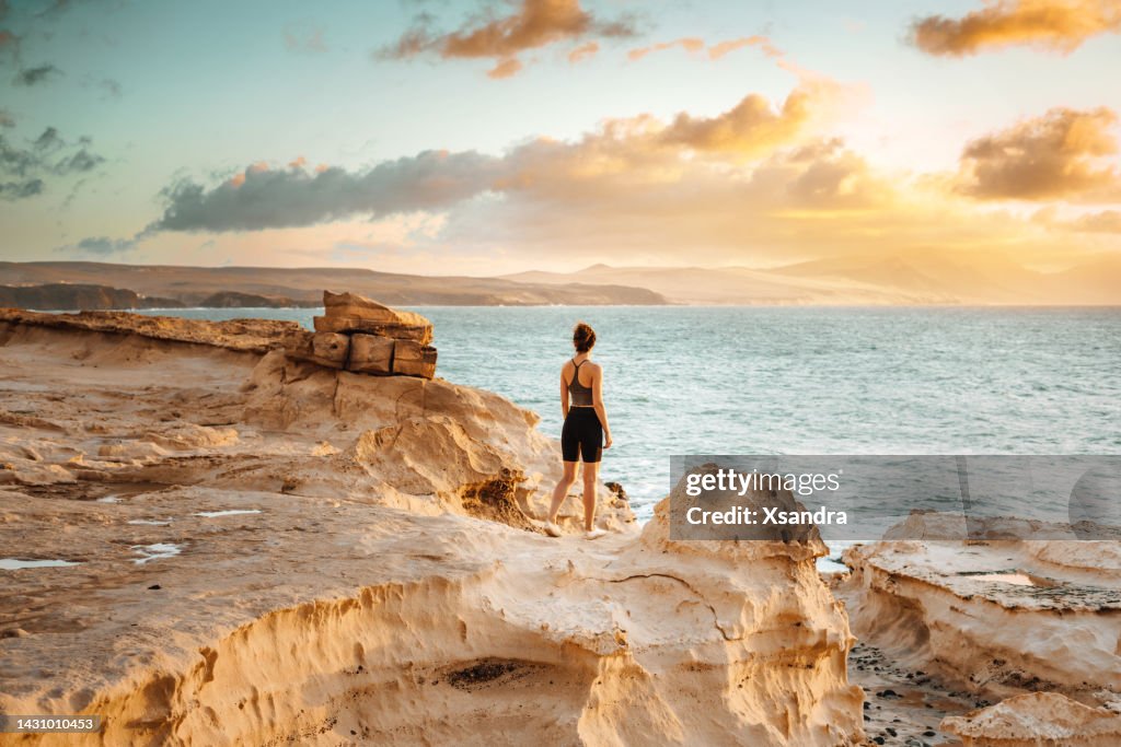 Frau steht auf einer Klippe mit Blick auf den spektakulären Sonnenuntergang