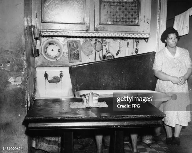 Woman standing beside a bathtub in a kitchen, with kitchen utensils hanging on the wall, living conditions in the Harlem neighbourhood of Manhattan...