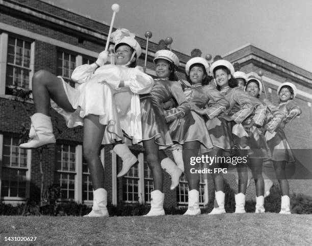 Low angle view of majorettes, with the leader majorette dressed in white leading a troupe in matching outfits, each standing with their right leg...