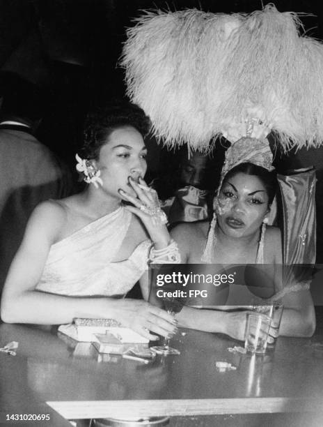 Helen Cleveland and an friend, with one smoking a cigarette, the other wearing a showgirl costume, at the Beaux-Arts Ball at the Savoy Ballroom in...