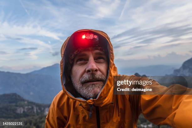 wanderer mit regenjacke und stirnlampe mit blick in den himmel in die berge - wandern regen stock-fotos und bilder