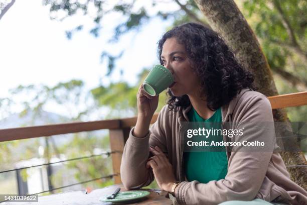 mujer latina bebiendo café en la terraza con vegetación - all people fotografías e imágenes de stock