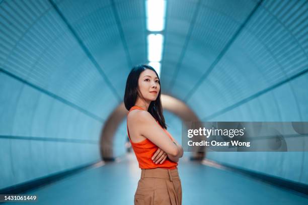 portrait of young asian woman with arms crossed standing in a futuristic tunnel - bold attitude stock pictures, royalty-free photos & images