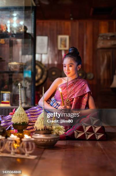 porträtfoto einer jungen schönen asiatischen laos-dame in traditionellen laotischen trachtenkleidern, die mit einer eleganten pose mit blumenstrauß und kerzen für das loy krathong-festival vor ihr sitzen - laos vientiane stock-fotos und bilder