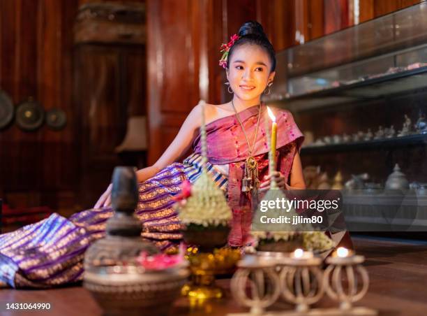 portrait photo of a young beautiful asian laos lady wearing traditional lao costume dresses sitting with an elegant pose with some flower bouquet and candles prepared for loy krathong festival in front of her - laos stockfoto's en -beelden