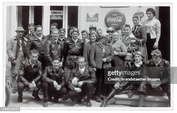 Snapshots. Group portrait of some motor-cycle drivers in front of a store. On the facade of the store some advertisement can be seen. Germany....
