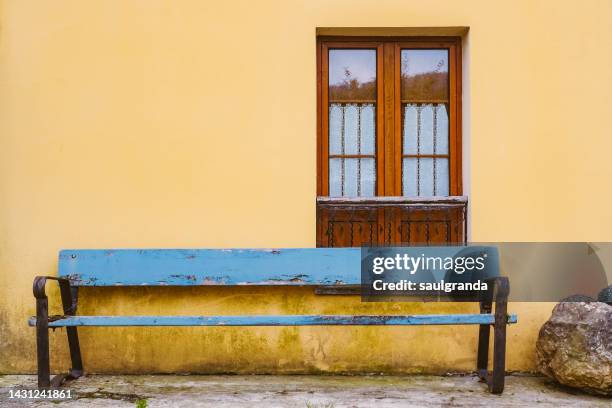 blue wooden bench in from of a yellow house - banco de españa fotografías e imágenes de stock