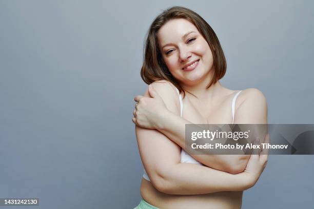 attractive oversize woman hugging oneself, posing on gray studio background - man touching shoulder stock-fotos und bilder