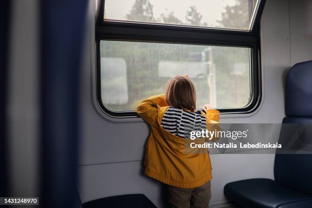 kid in yellow jacket on train look out window. back view. calm. - kid sitting stock pictures, royalty-free photos & images