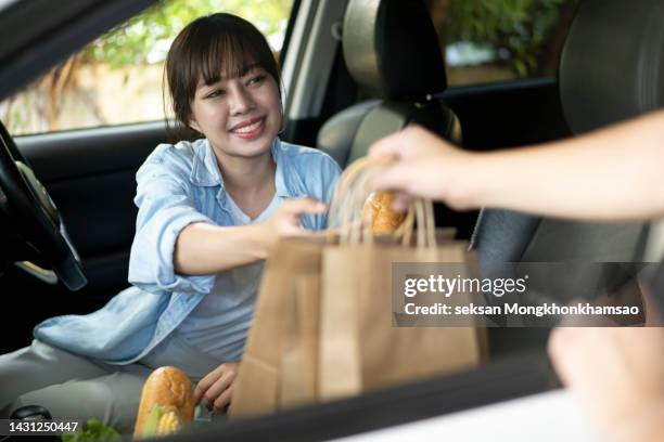 young woman smiles as she gets food on the way into the car. - カーブサイドピックアップ ストックフォトと画像