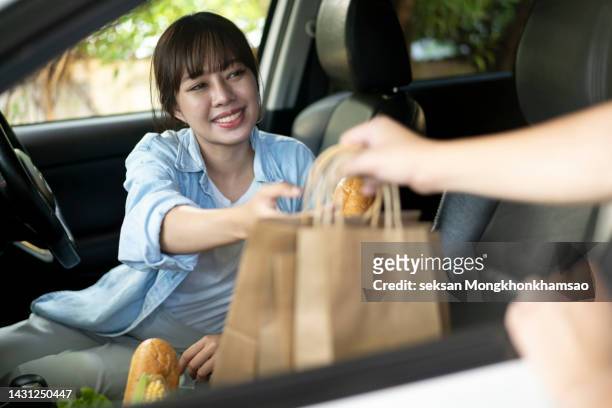 young woman smiles as she gets food on the way into the car. - curbside pickup 個照片及圖片檔