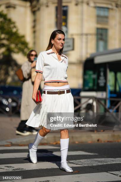 Camille Charriere wears diamonds earrings, a gold long chain pendant necklace, a white striped print pattern / short sleeves / blue and red striped...