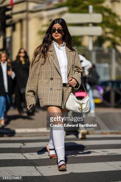 Ola Farahat wears black sunglasses, a white shirt, a beige and brown / black houndstooth print pattern oversized jacket, a matching beige and brown /...