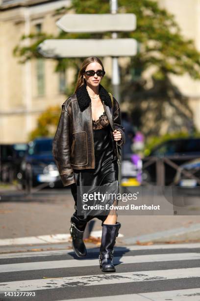 Pernille Teisbaek wears black sunglasses, silver and gold earrings, a diamonds necklace, a dark brown shiny leather with black sheep collar oversized...