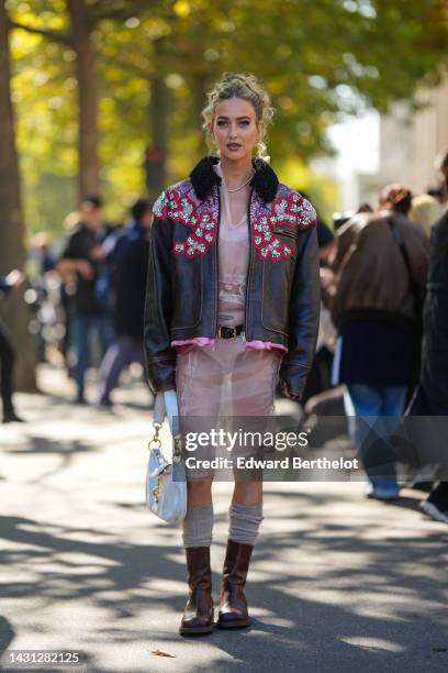 Emili Sindlev wears gold earrings, a diamonds necklace, a pale pink tulle with embroidered flower pattern knees dress from Miu Miu, a dark brown...