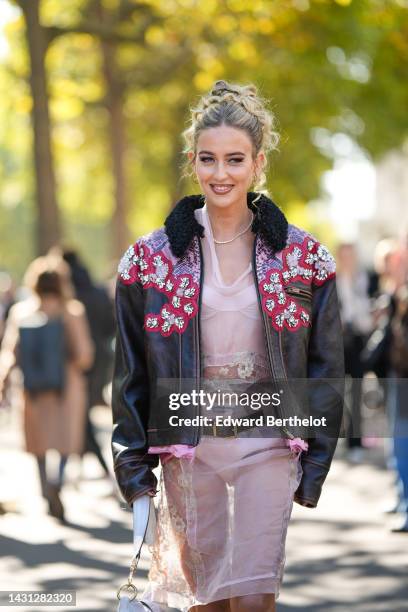 Emili Sindlev wears gold earrings, a diamonds necklace, a pale pink tulle with embroidered flower pattern knees dress from Miu Miu, a dark brown...