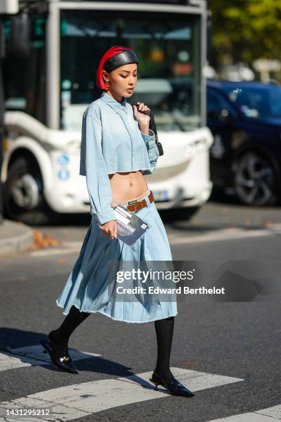 Kiwi Lee wears a black shiny leather nailed / studded large headband, gold large earrings from Miu Miu, a pale blue denim cropped shirt from Miu Miu,...