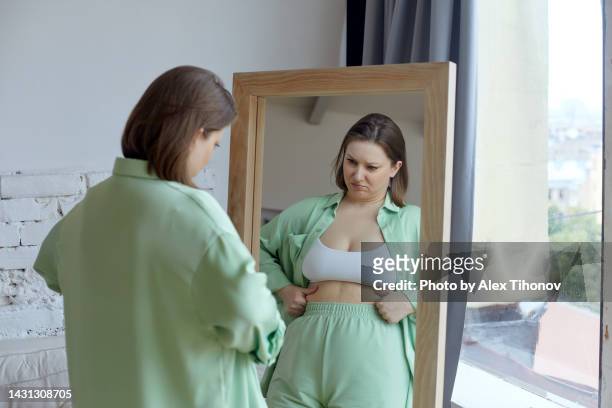 size plus woman looking by reflection in mirror feels frustrated and dissatisfied by overweight - overweight imagens e fotografias de stock