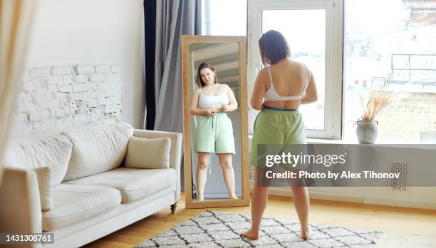 woman measures her waist at home - woman-looking-into-mirror-full-body stock pictures, royalty-free photos & images