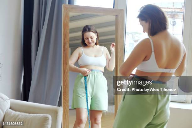 oversize woman measures her waist size at home feels satisfied - gewicht verlieren stock-fotos und bilder