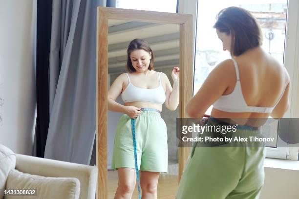 oversize woman measures her waist size at home feels satisfied - high waist stockfoto's en -beelden