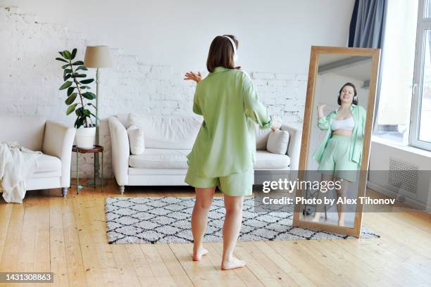 plus size woman holds smartphone, listen music through headphones, dancing standing barefoot in living room - fat woman dancing stockfoto's en -beelden