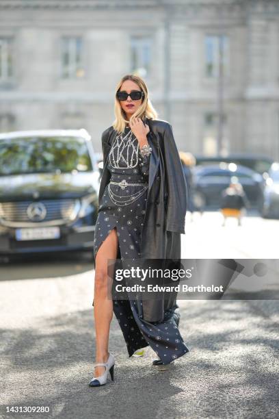 Candela Novembre wears black sunglasses from Chanel , a black shiny leather long coat, a black with white logo print pattern with embroidered crystal...