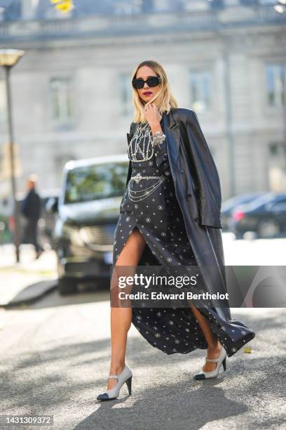 Candela Novembre wears black sunglasses from Chanel , a black shiny leather long coat, a black with white logo print pattern with embroidered crystal...