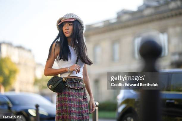 Yoyo Cao wears a pale gray braided wool and brown shiny leather beret cap, gold earrings, a white tank-top, a black shiny leather crossbody bag from...