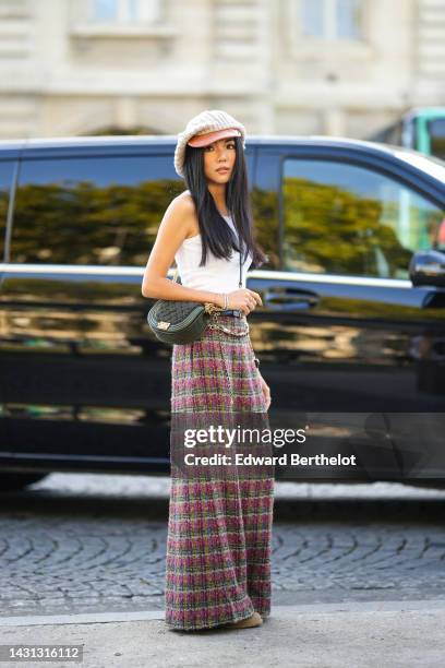 Yoyo Cao wears a pale gray braided wool and brown shiny leather beret cap, gold earrings, a white tank-top, a black shiny leather crossbody bag from...