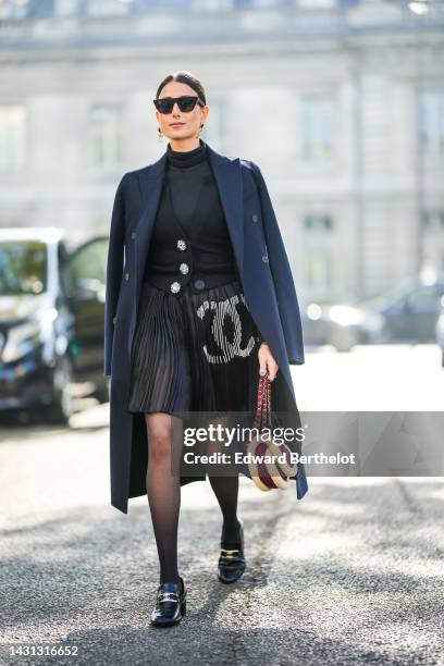 Julia Haghjou wears black sunglasses, a black turtleneck pullover, a black wool with rhinestones large buttoned cardigan, a navy blue long coat, a...