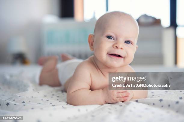 joyful little baby boy laying on front on bed. - blond boy stockfoto's en -beelden