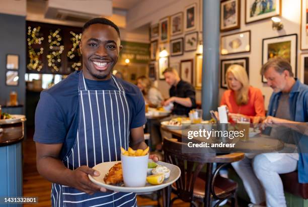 happy waiter serving food at a pub - black apron stock pictures, royalty-free photos & images