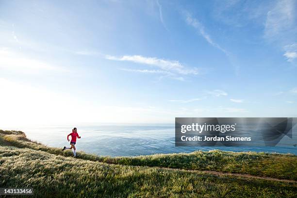 woman trail running near the ocean. - distant people stock pictures, royalty-free photos & images