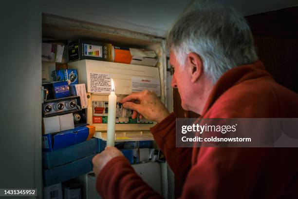 senior man checking home fuse box by candlelight during power outage - fuse box stock pictures, royalty-free photos & images