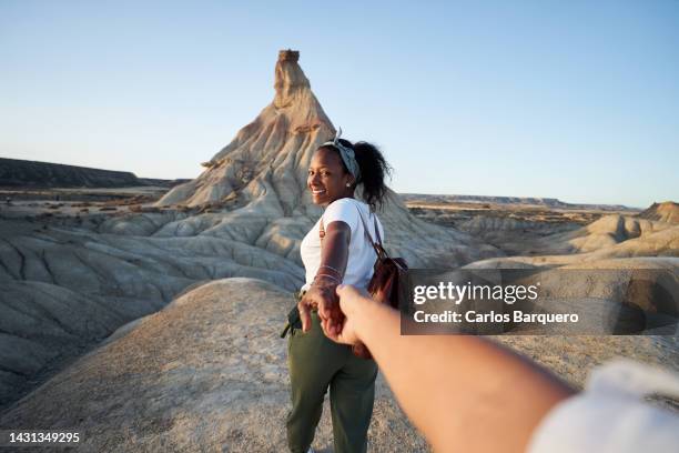 personal perspective of happy black woman guiding her partner to explore a desert, holing hands. - couple dunes stock-fotos und bilder