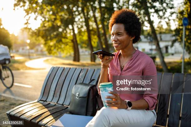 businesswoman relaxing on the bench on the city street, enjoying a coffee break from work - conference phone stock pictures, royalty-free photos & images