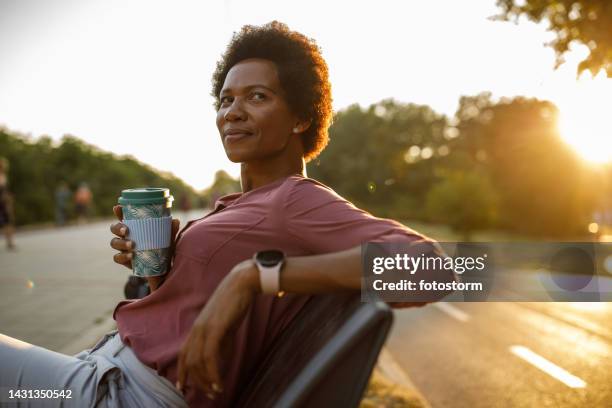 businesswoman relaxing on the bench on the city street, enjoying a coffee break from work - golden hour woman stock pictures, royalty-free photos & images