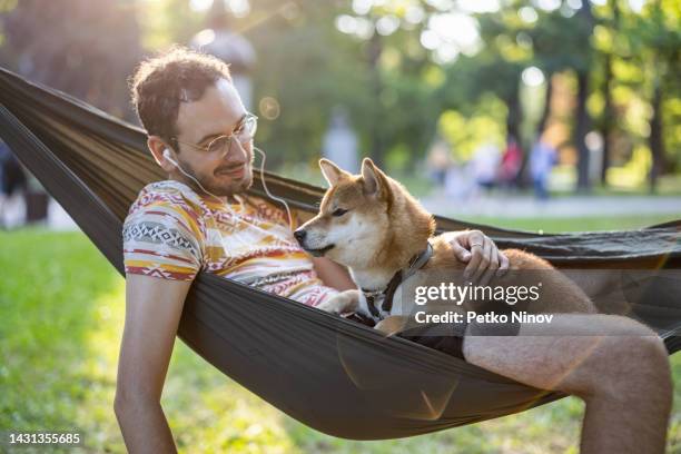man is petting his dog in a hammock - young man listening music and relaxing in hammock stock pictures, royalty-free photos & images