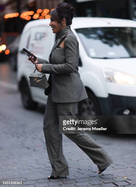 Guest is seen a grey suit blazer with cut-outs and a matching suit pants, grey Hermès Kelly mini bag and black heels, outside Gauchere, during Paris...