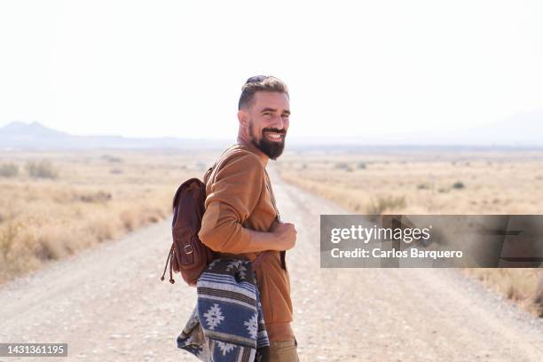 handsome blond man at desert road, looking at camera. - itinerant stock-fotos und bilder