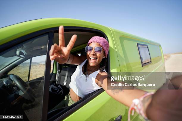 cheerful black woman taking selfie in car through smart phone during weekend road trip at desert. - mensaje de móvil fotografías e imágenes de stock