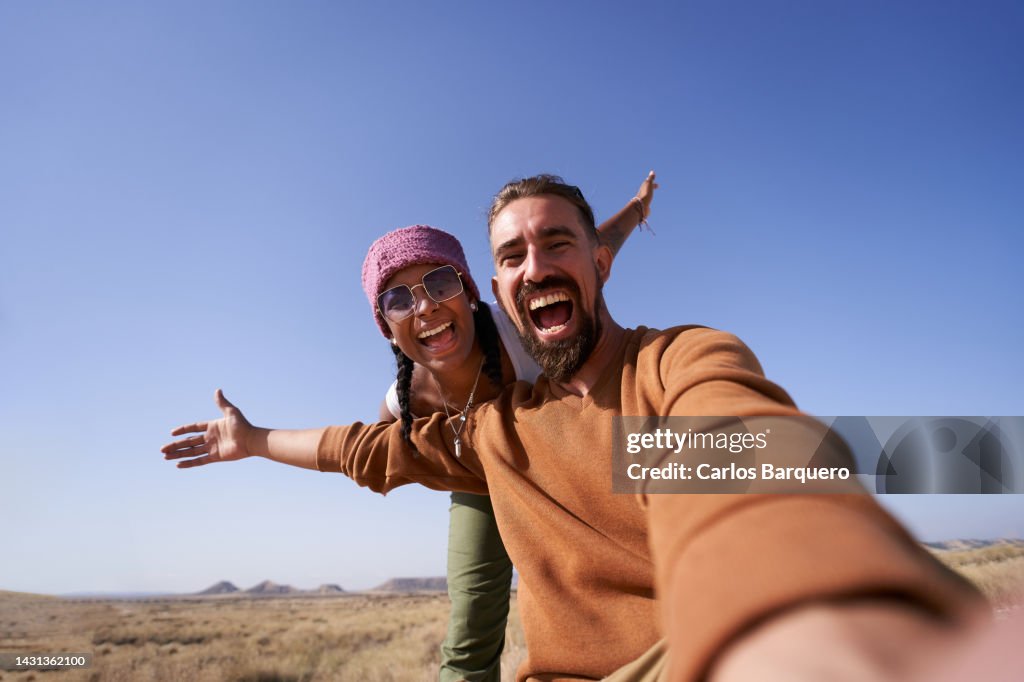 Enthusiastic photo of nomadic couple taking a selfie showing the desert to post it on social media apps.
