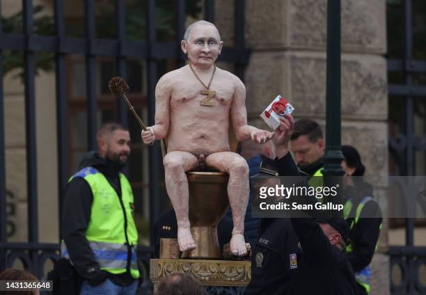 Man replaces a toy washing machine covered in red paint in the hand of an effigy of a naked Russian President Vladimir Putin sitting on a golden...