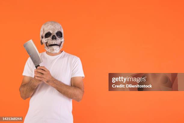 man wearing skull mask and white t-shirt, holding a knife, with copy space, celebrating halloween, on an orange background. concept of celebration, day of the dead, all saints' day and carnival. - cover monster face stock pictures, royalty-free photos & images